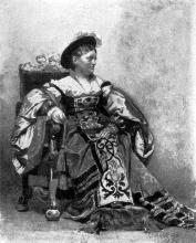 Sitzende Dame im Kostüm mit einem Fuß auf dem Hocker